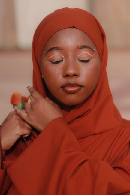 Close-up portrait of a woman in a red hijab with elegant makeup and closed eyes, exuding tranquility.