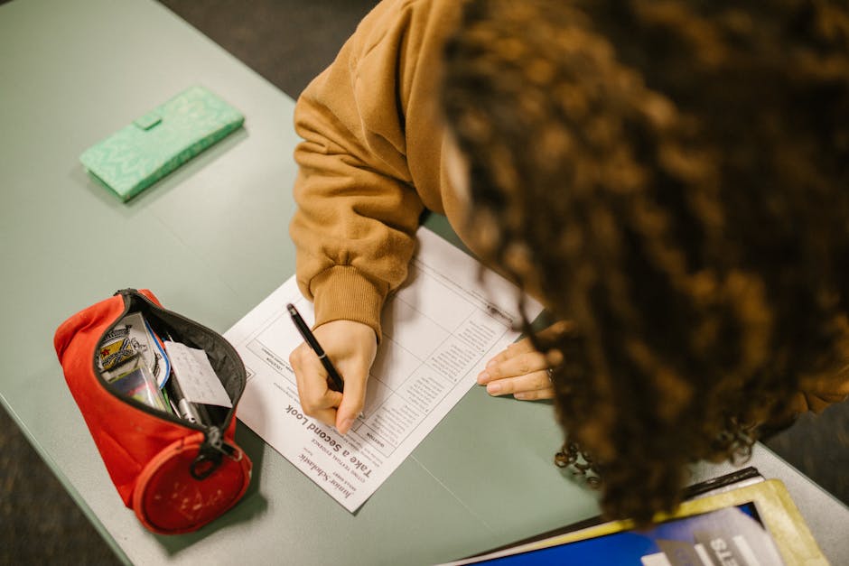 Overhead shot of a student writing during an exam at school with a pencil case on the desk.