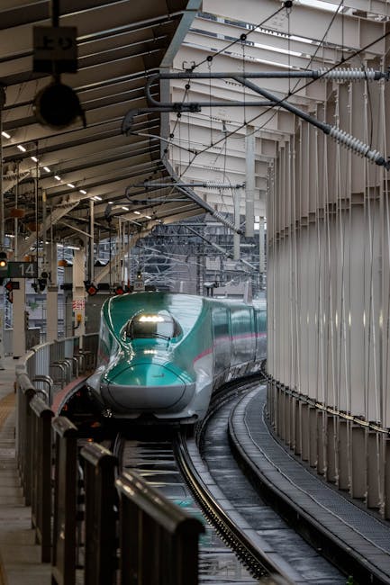 A sleek green Shinkansen bullet train arriving at a contemporary Japanese train station platform.