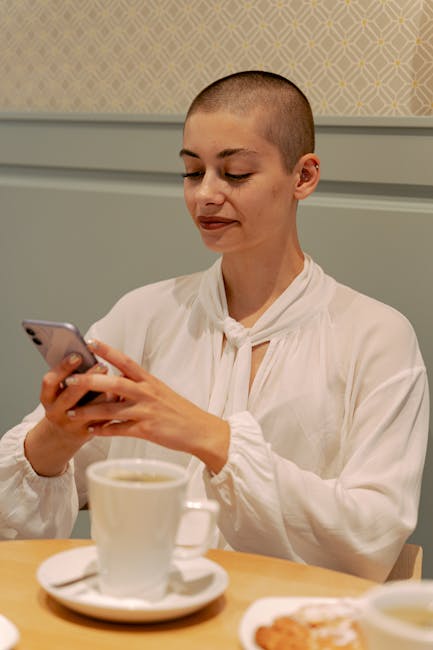 Bald woman with smartphone enjoying a coffee in a modern cafe, exuding calmness.