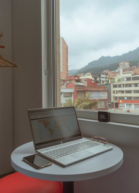 Laptop and phone on a table with a view of Bogotá cityscape through a window.