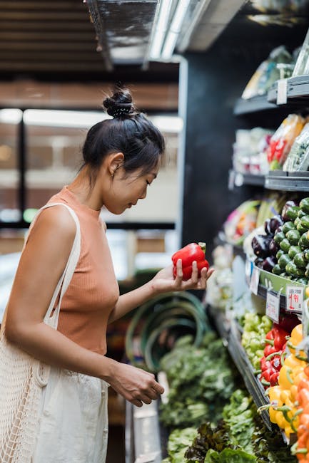 A woman carefully selects fresh vegetables in a grocery store aisle.