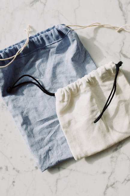 Top view of white and blue fabric eco friendly sacks with drawstrings placed on each other on white marble surface in light room