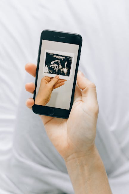 A hand holding a smartphone displaying a pregnancy ultrasound image.