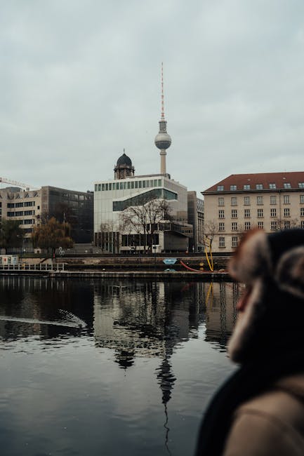 The iconic Berlin TV Tower reflected in a river with urban surroundings.