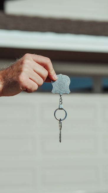A close-up image of a hand holding a key with keychain outdoors, symbolizing new home or rental purchase.