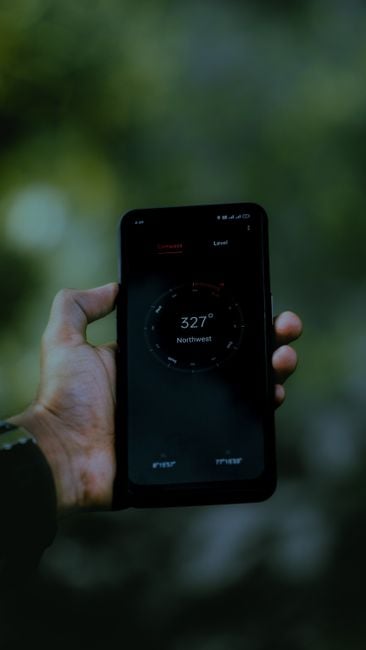 A person holding a smartphone displaying a compass app. The device shows a northwest direction reading at 327 degrees.