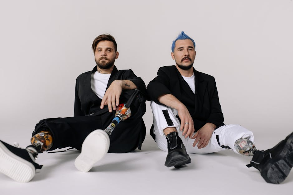 Two stylish men with prosthetic legs sitting in a studio, embodying modern fashion and empowerment.