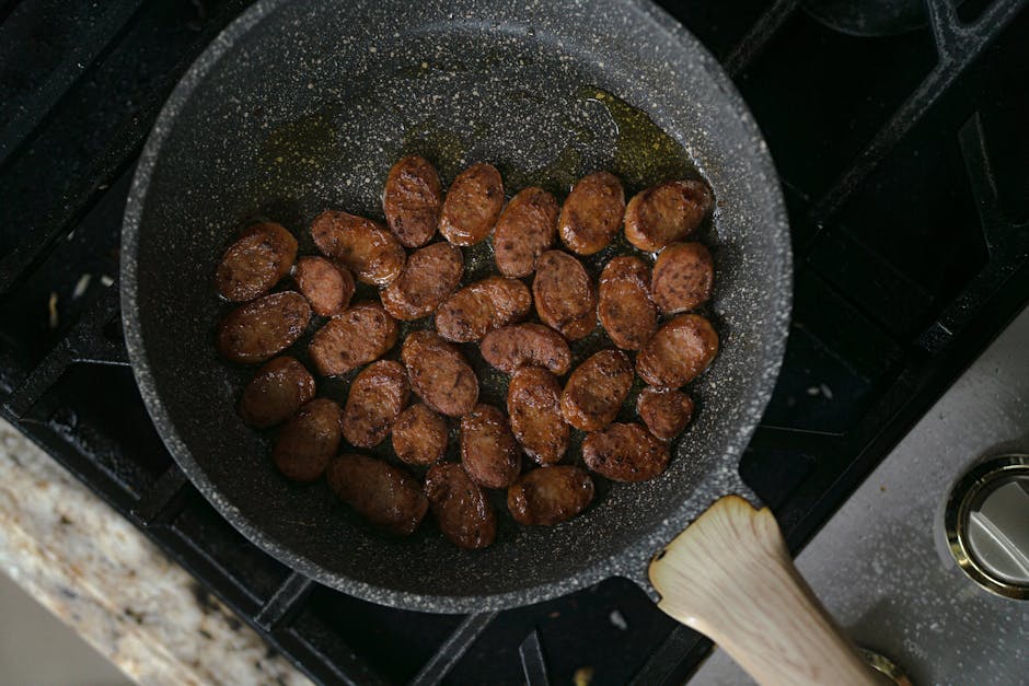 A mouth-watering view of sliced sausages cooking in a frying pan on a stove.