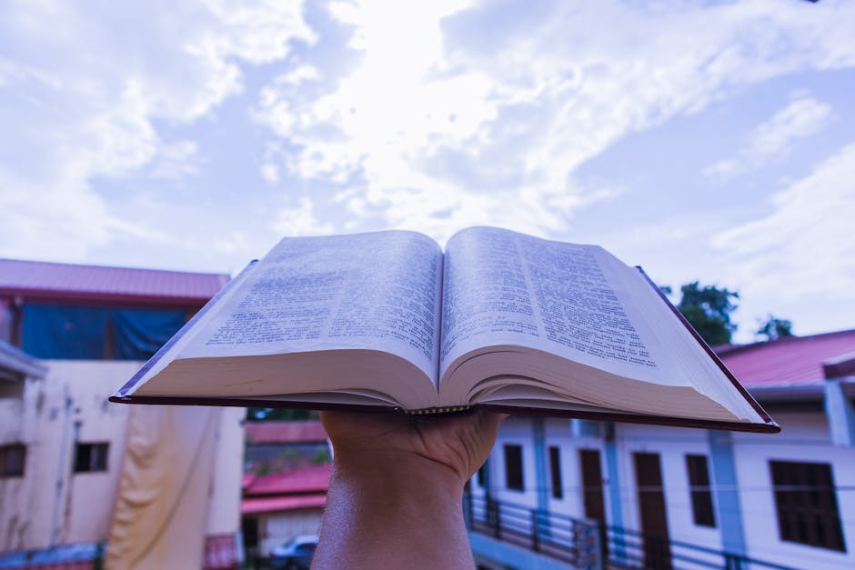 Hand holding an open book outdoors with clear blue sky as the background.