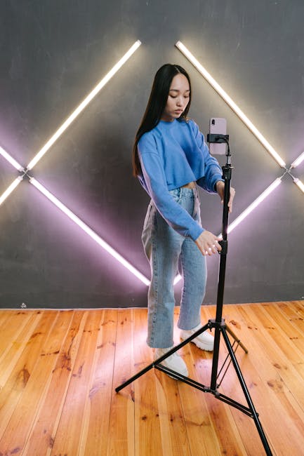 Asian woman adjusts smartphone on tripod in modern studio for content creation.