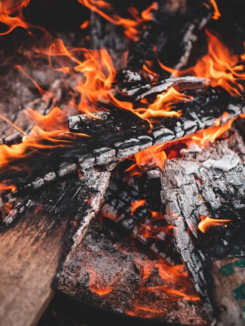 A close-up of vibrant flames engulfing charred firewood, showcasing the energy and warmth of a campfire.