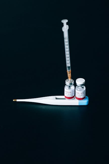 Close-up of COVID-19 vaccine vials and syringe with a digital thermometer on a dark background.