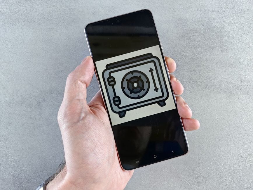 Close-up of a smartphone showing a safe icon held in a hand, symbolizing digital security.