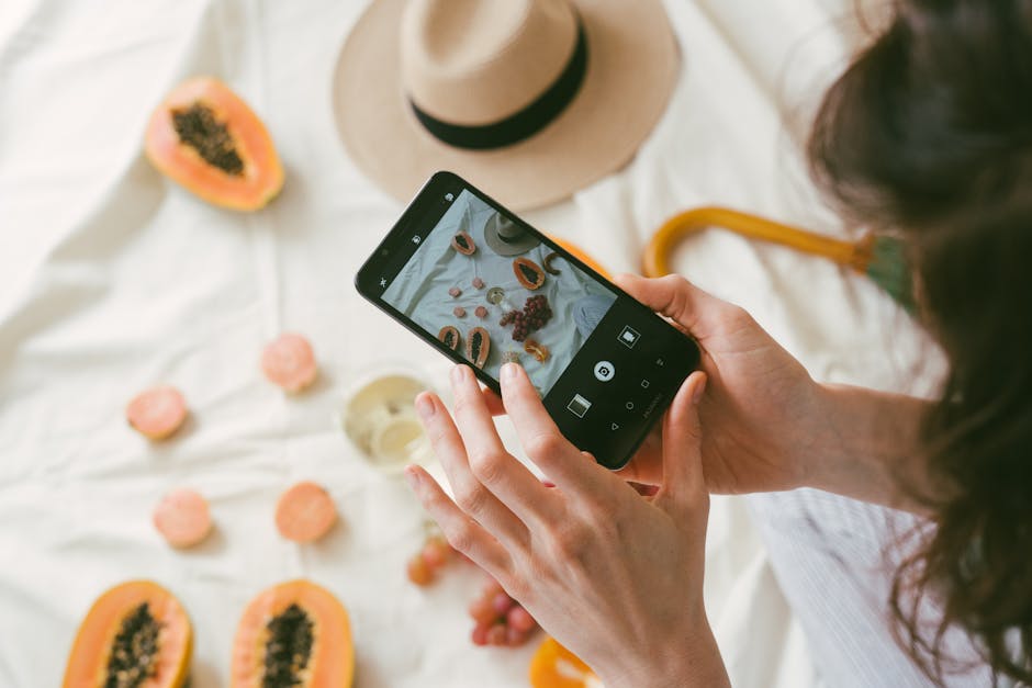 A person uses a smartphone to photograph an artistic arrangement of fresh fruits on a table.