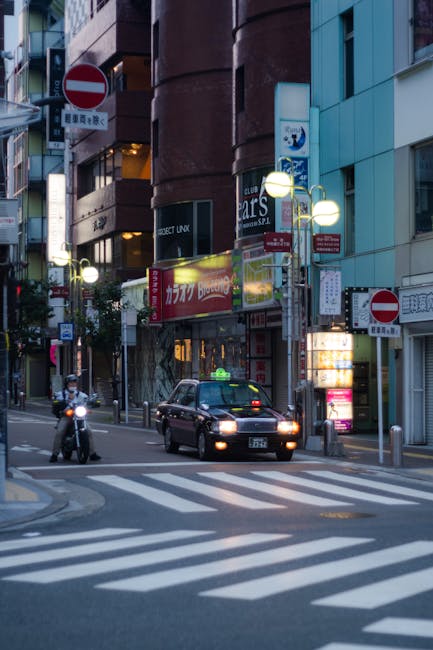 A bustling street in Fukuoka at night featuring a taxi and vibrant city lights.