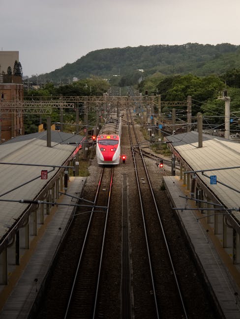 High-speed train arriving at Hsinchu Station in Taiwan, surrounded by lush greenery and hills.