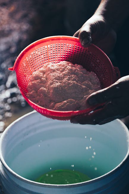 High angle of crop anonymous person filtering cottage cheese with whey through colander while preparing homemade cheese