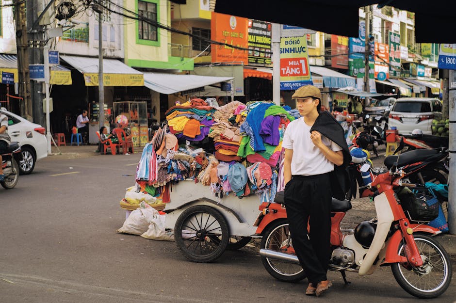 Man by a street vendor cart with colorful clothes in a lively city street.