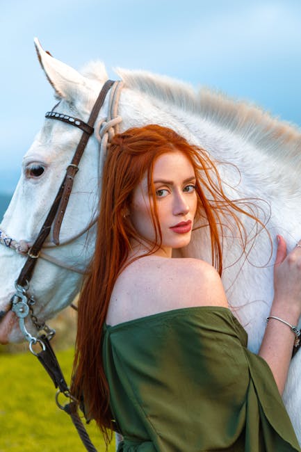 A redhead woman embraces a white horse in a lush green landscape, showcasing beauty and nature.
