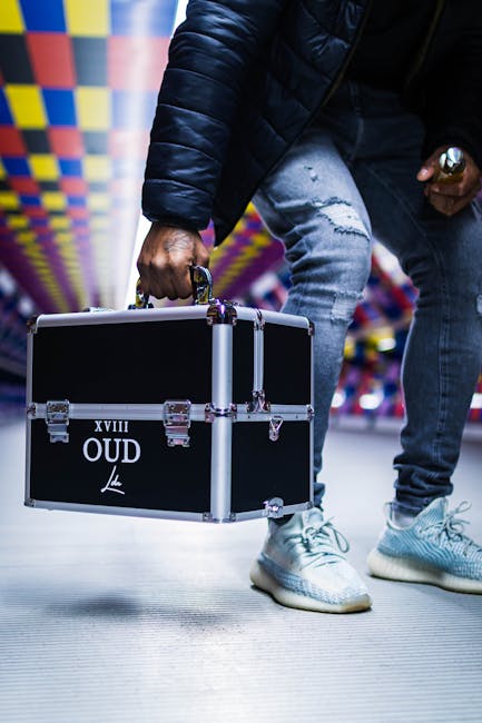 A man in a vibrant corridor holds a black metal suitcase labeled 'XVIII OUD'.