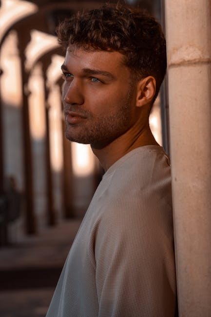 Portrait of a contemplative man leaning against a pillar, bathed in sunset light.