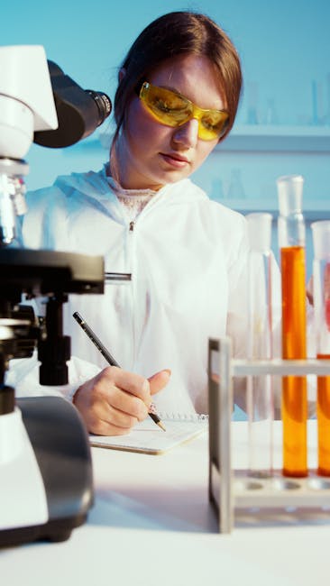 A female scientist writes notes in a lab among test tubes and a microscope.