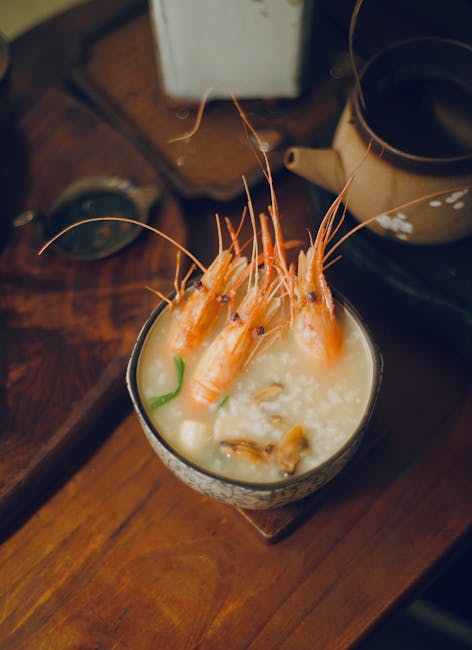 A gourmet seafood dish featuring shrimp in rich broth, served elegantly with a tea set.