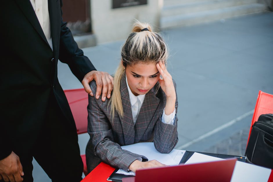 Businesswoman in stress at outdoor table, seeking support from colleague.