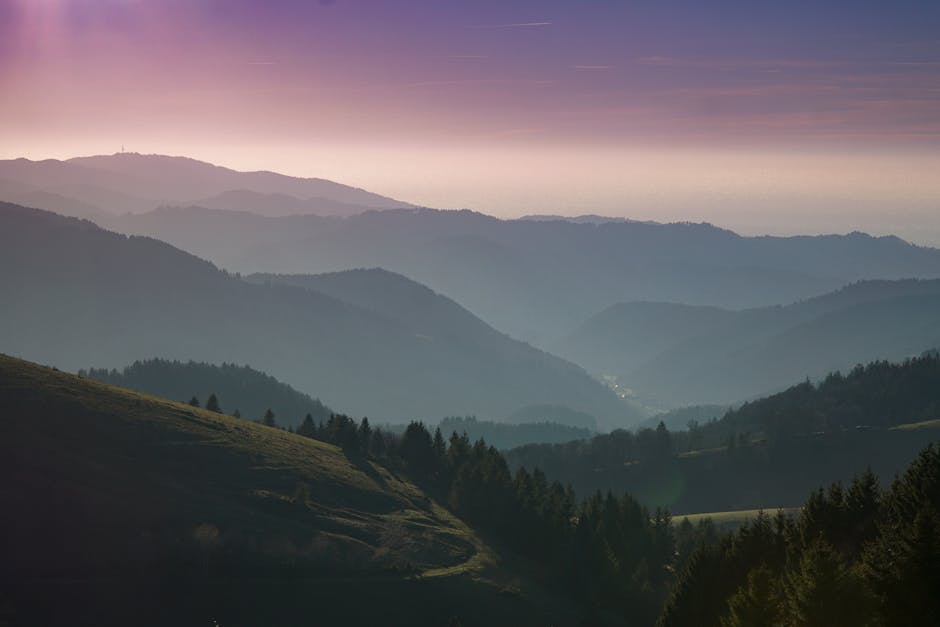 A beautiful view of rolling hills and forests under a colorful sunset sky.