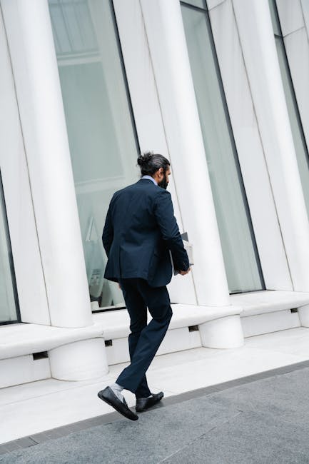 Professional man in full suit walking past modern building facade, embodying urban business life.