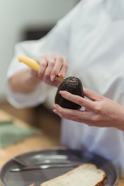 Close-up of hands peeling an avocado in a kitchen setting, showcasing food preparation.
