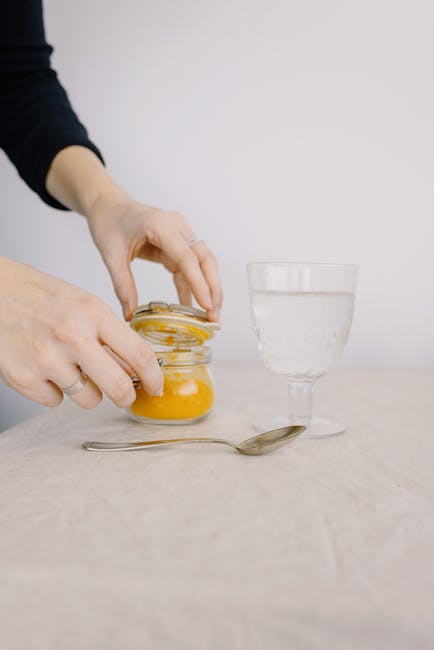 Hands preparing a drink with orange powder and glass of water on table.