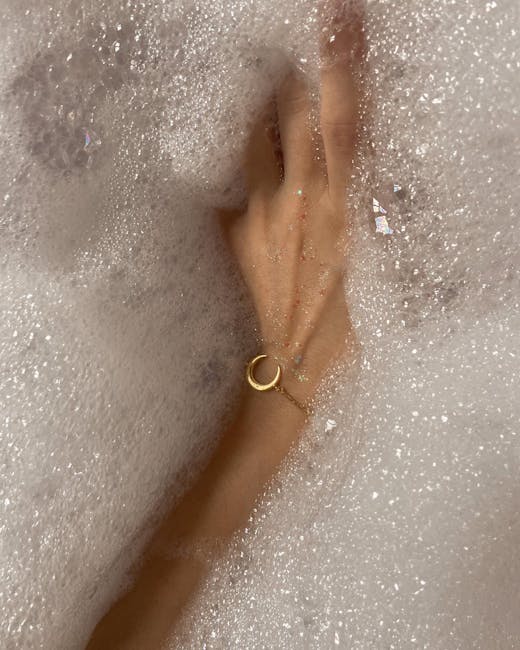 A woman's hand with a bracelet submerged in a bubbly bathtub, capturing serenity and self-care.