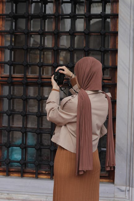 A woman in a hijab photographs a city scene with a DSLR camera.