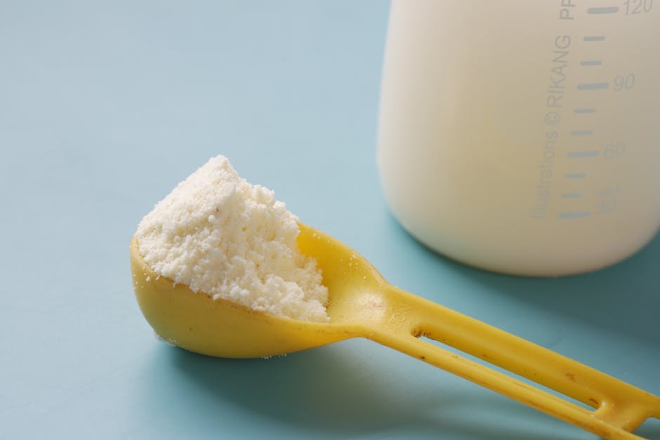 A yellow spoon filled with powdered milk, next to a measuring bottle, on a blue background.