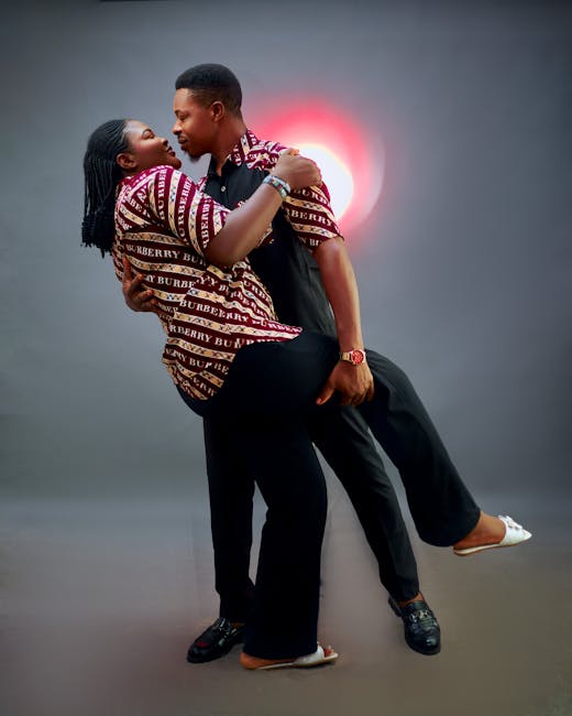 Couple in stylish outfits dancing closely, captured in studio with dramatic lighting.
