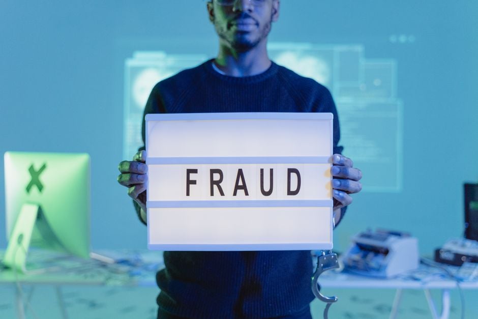 A man holding a sign reading 'FRAUD' in a tech environment, highlighting cybersecurity concerns.