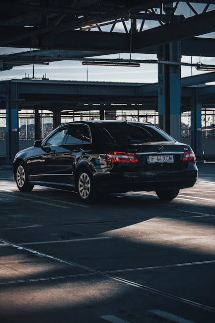 Elegant black Mercedes-Benz E-Class parked in a contemporary urban garage with shadows enhancing its sleek design.