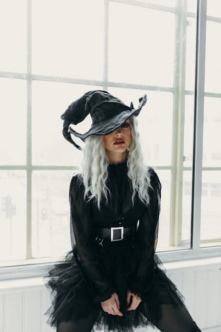 Stylish woman in witch costume poses indoors, embodying elegance and mystery.
