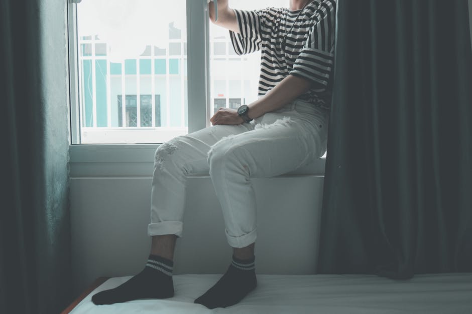 A stylishly dressed man seated by a window in an indoor setting, creating a serene vibe.