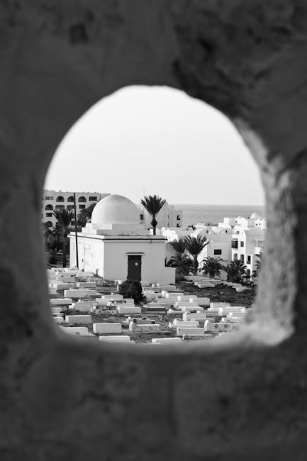 Black and white photo of mosque and buildings seen through an archway.