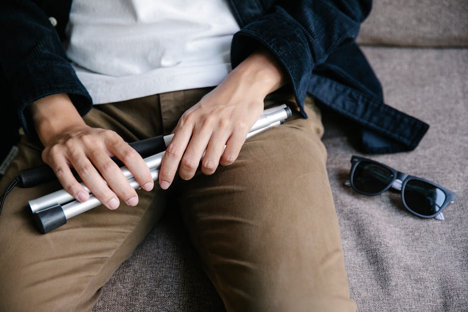 Close-up of a person holding a white cane with sunglasses on a sofa. Emphasizes accessibility.
