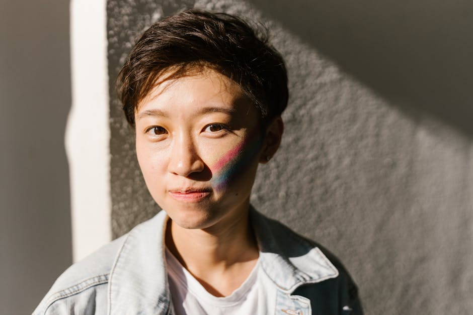 Portrait of a young adult with rainbow makeup on face, in casual attire.