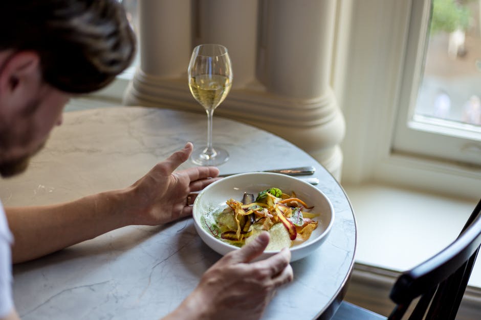A stylish dining scene featuring a gourmet meal and a glass of white wine by a window.