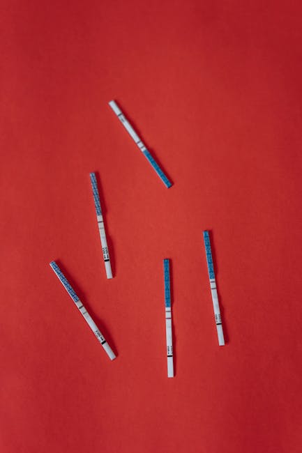 Multiple pregnancy test strips scattered on a vibrant red backdrop, symbolizing fertility and anticipation.