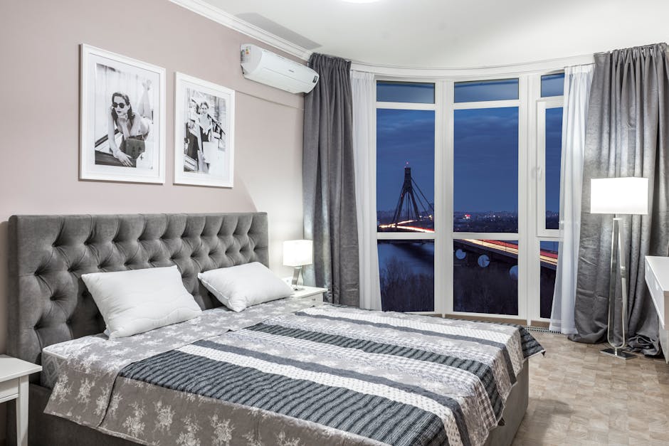 A cozy bedroom with a modern design featuring a cityscape view through large windows.