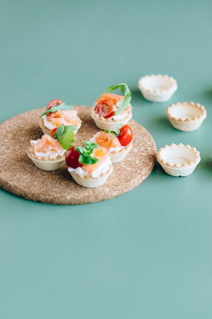 Top-down view of assorted savory mini tarts with fillings on a green background.
