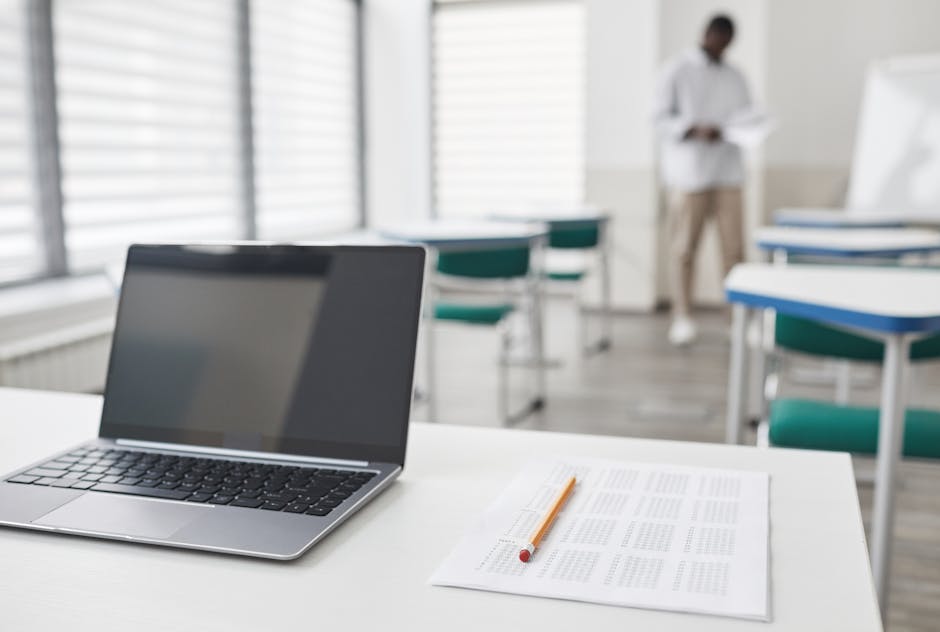 Laptop and exam sheet on a desk in a modern classroom setting.