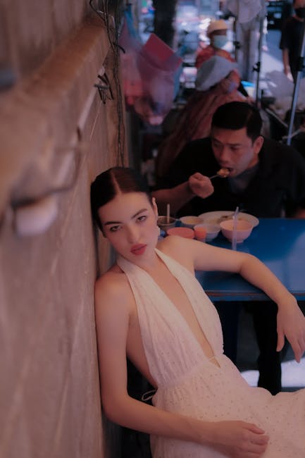 Woman in elegant dress poses in vibrant Bangkok street food scene.